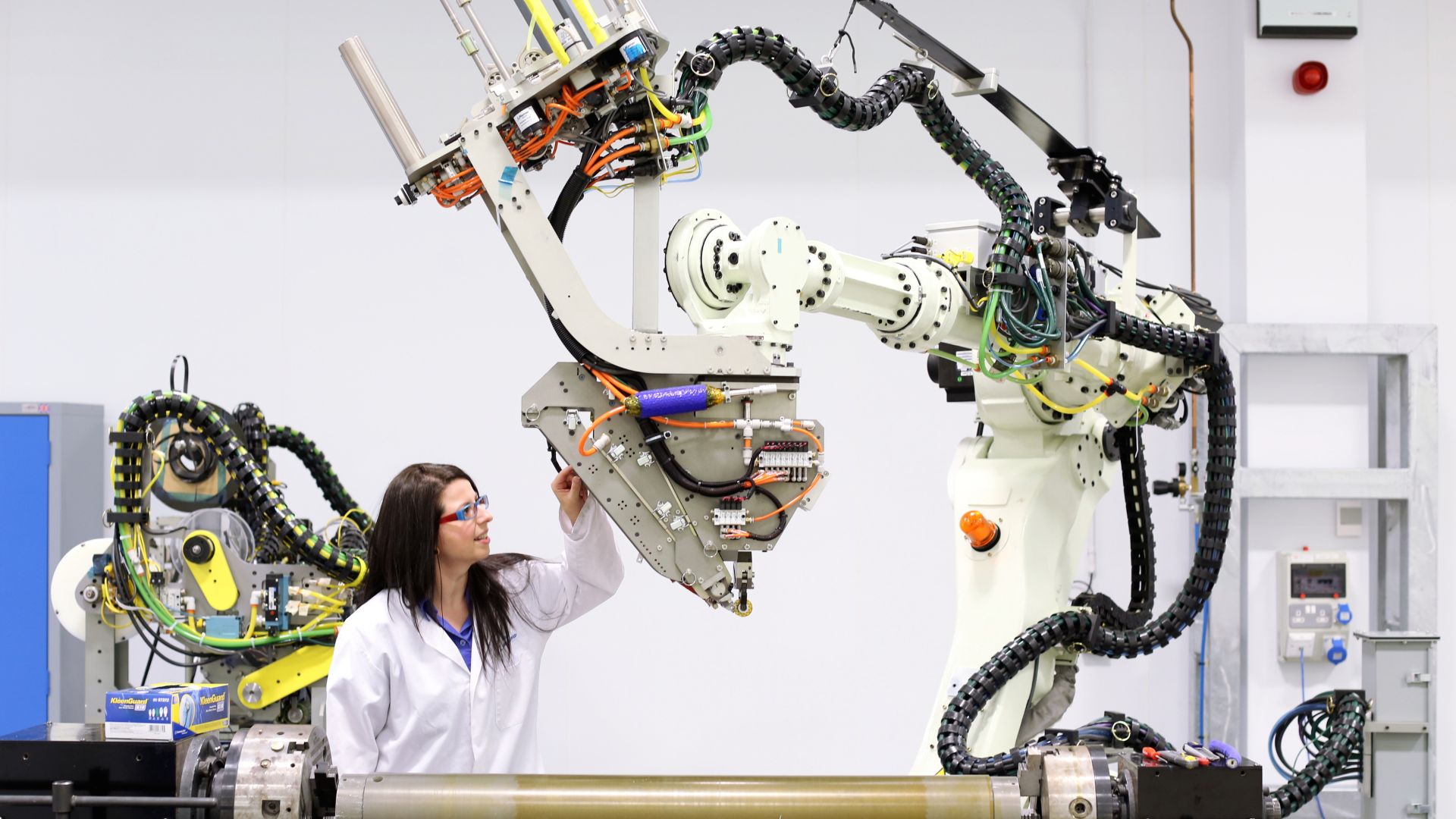 Girl wearing a white scientific robe, standing next to a large robotic device